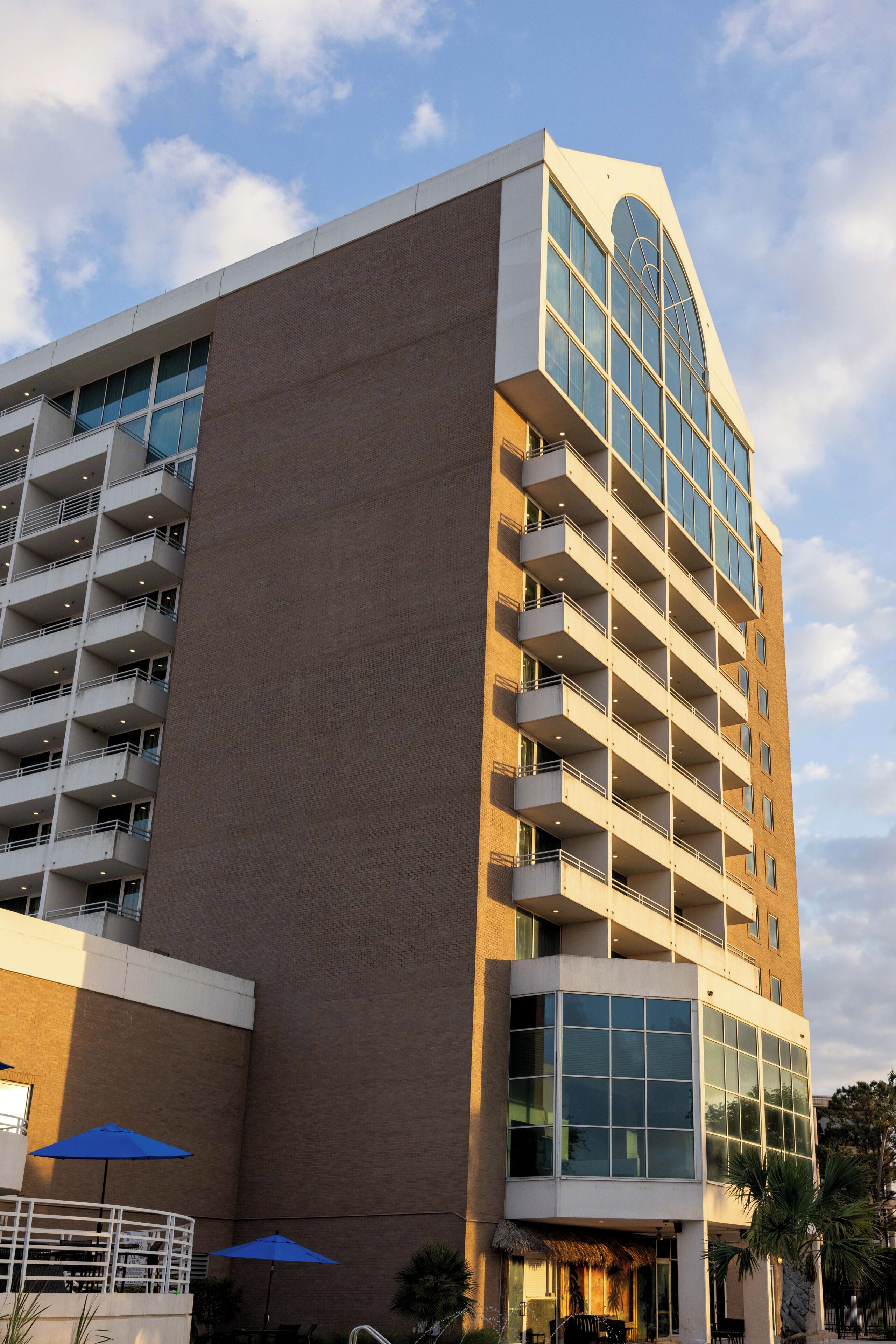 A multi-story hotel with a prominent glass facade, balconies on each floor, and a central entrance with a covered area.