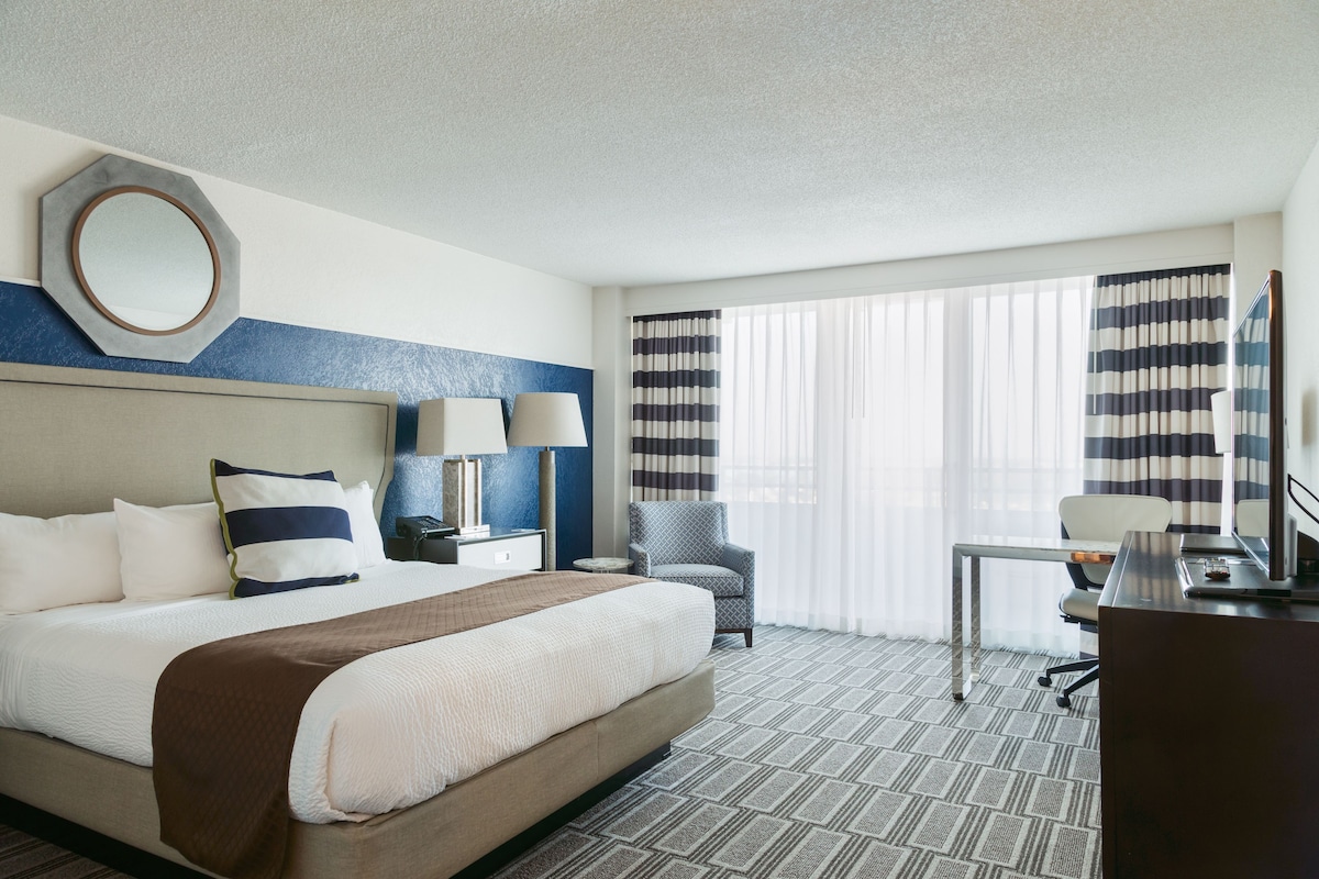 A hotel room with a large bed, a desk, a chair, and a TV.