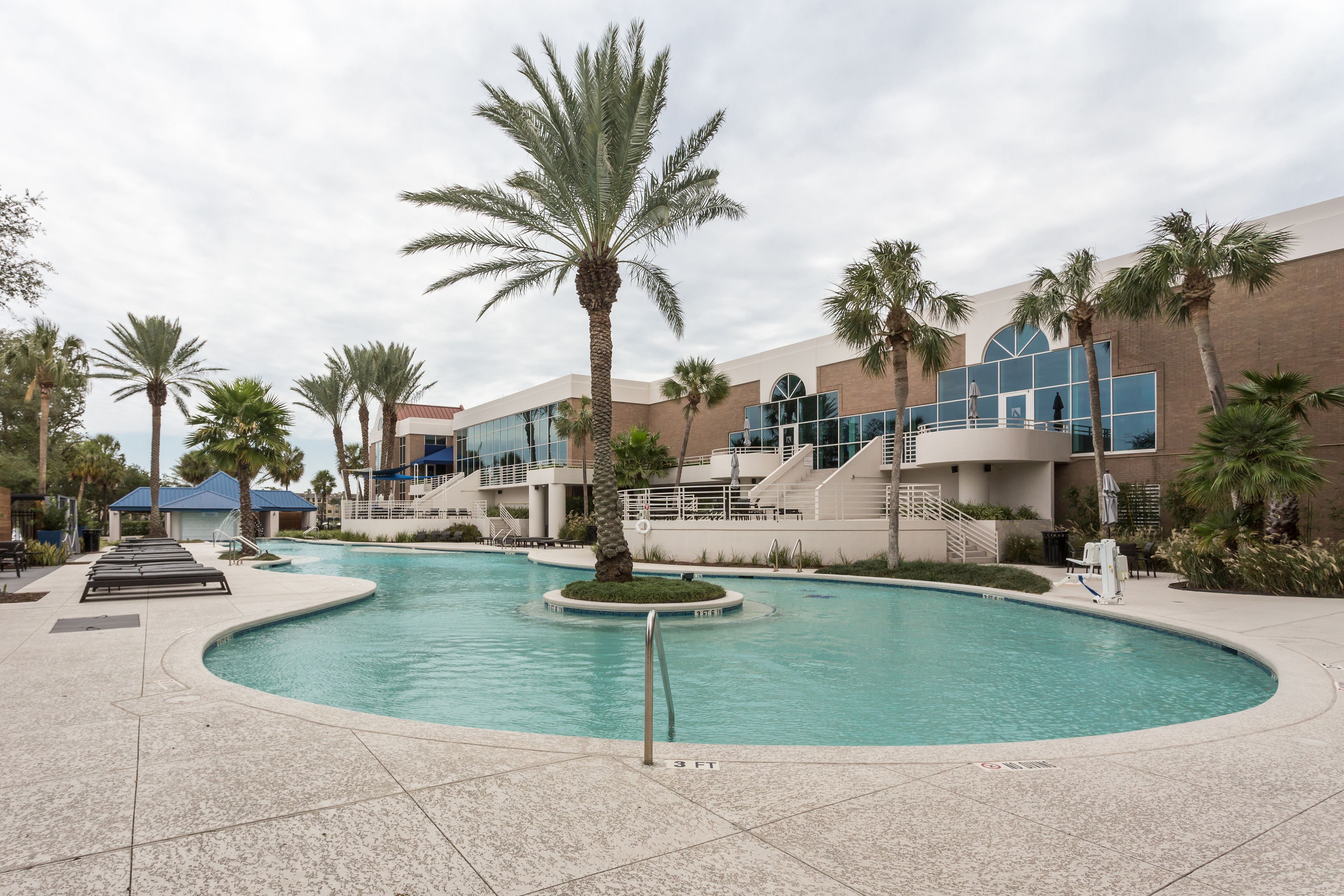 A swimming pool with palm trees, a covered area, and a building with a modern design.