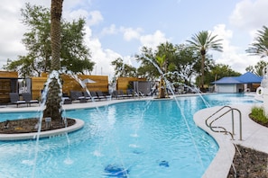 Piscina com recursos aquáticos, espreguiçadeiras e palmeiras.