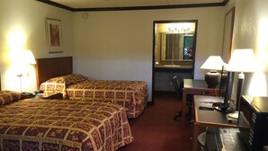 Ein Hotelzimmer mit zwei Betten, einem Schreibtisch, einem Stuhl, einem Spiegel und einer Lampe.