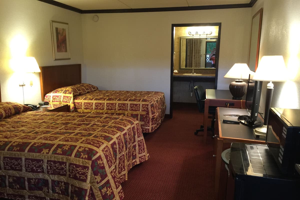 Quarto de hotel com duas camas, uma escrivaninha, uma cadeira, um espelho e uma luminária.