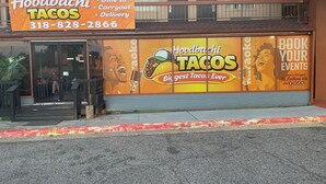 Ein Schaufenster mit einem Schild für Hoodbachi Tacos, das Speisen zum Essen vor Ort, zum Mitnehmen und Lieferservice anbietet.