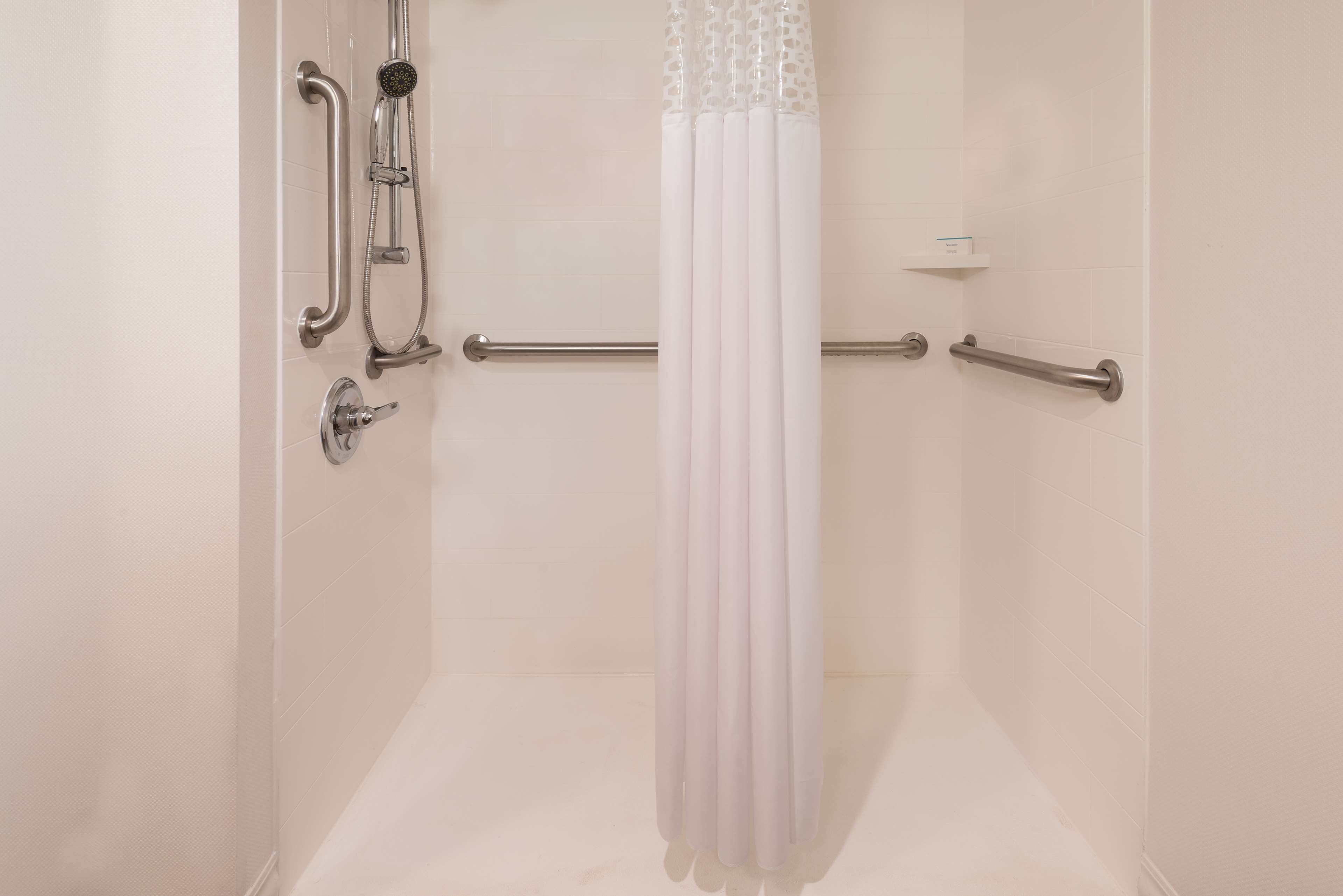 Ducha con cortina blanca, barras de apoyo y cabezal de ducha de mano.