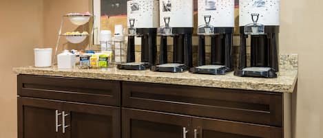 A coffee station with multiple dispensers, a coffee pot, and a sugar dispenser on a granite countertop.