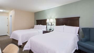 A hotel room with two beds, a chair, a nightstand with a lamp, and a phone.