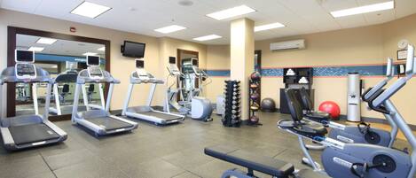 Un gimnasio con cintas de correr, elípticas y equipo de levantamiento de pesas.