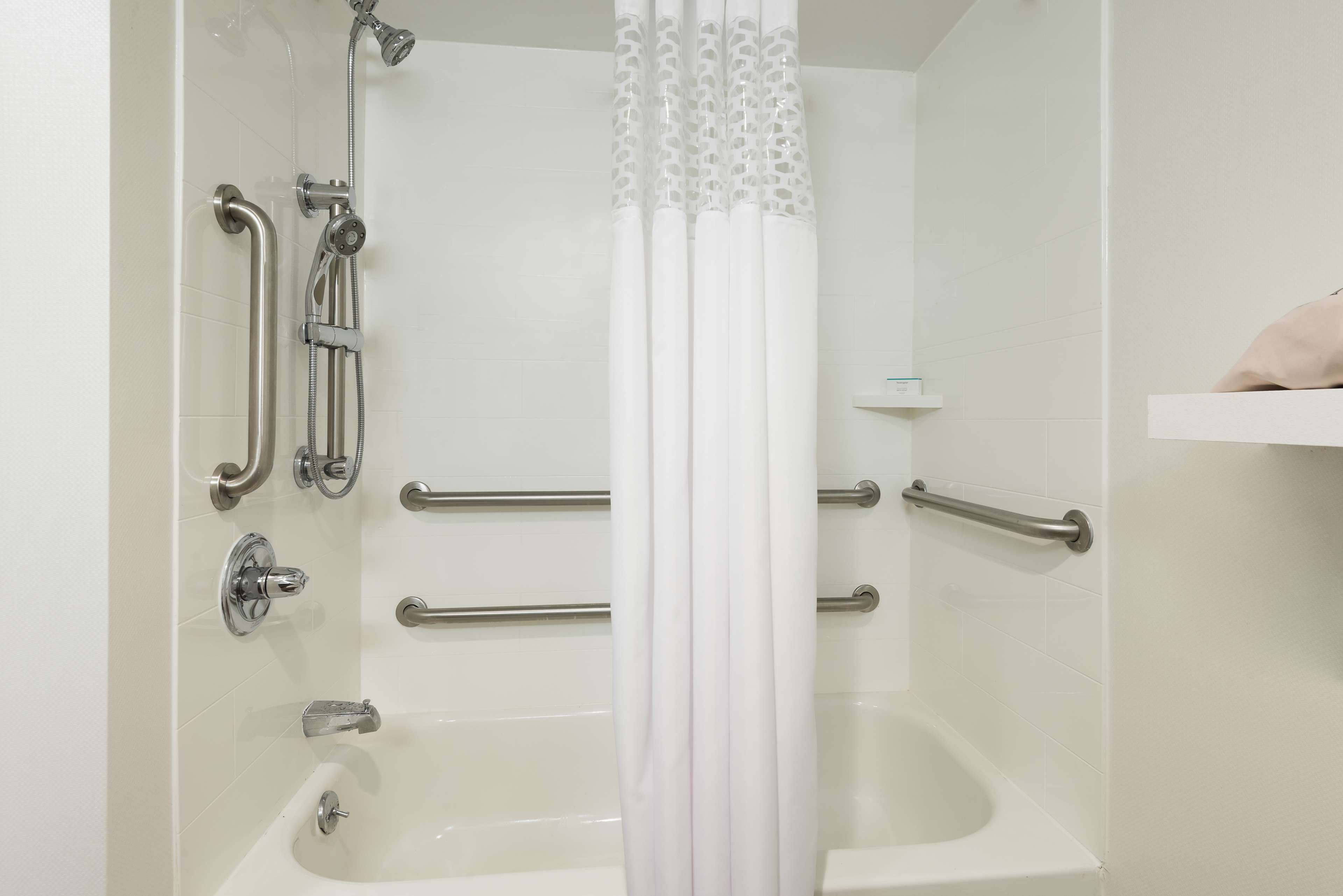 Une salle de bain équipée d’une baignoire, de barres d’appui et d’un rideau de douche.
