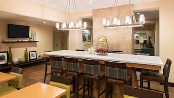 A hotel dining area with a long communal table, multiple chairs, and a television mounted on the wall.