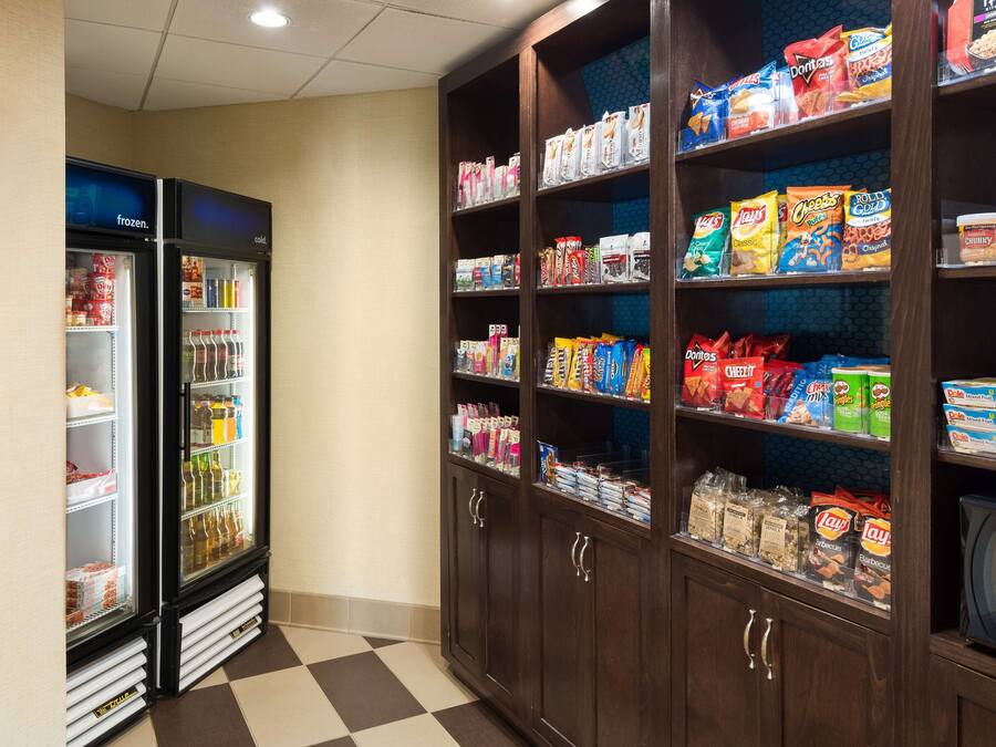 Zona de venta automática con refrigerador y estantes llenos de diversas bebidas y aperitivos.