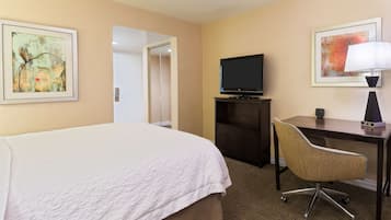 Habitación de hotel con una cama grande, un escritorio con silla, un televisor y dos obras de arte enmarcadas en las paredes.