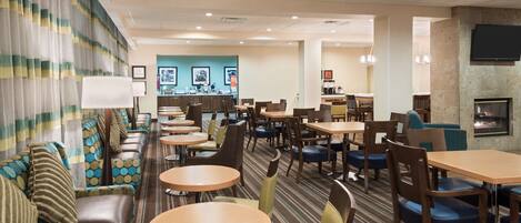 A hotel lobby with seating areas, tables, a reception desk, and a TV mounted on the wall.