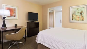 A hotel room with a bed, desk, chair, TV, and artwork on the walls.