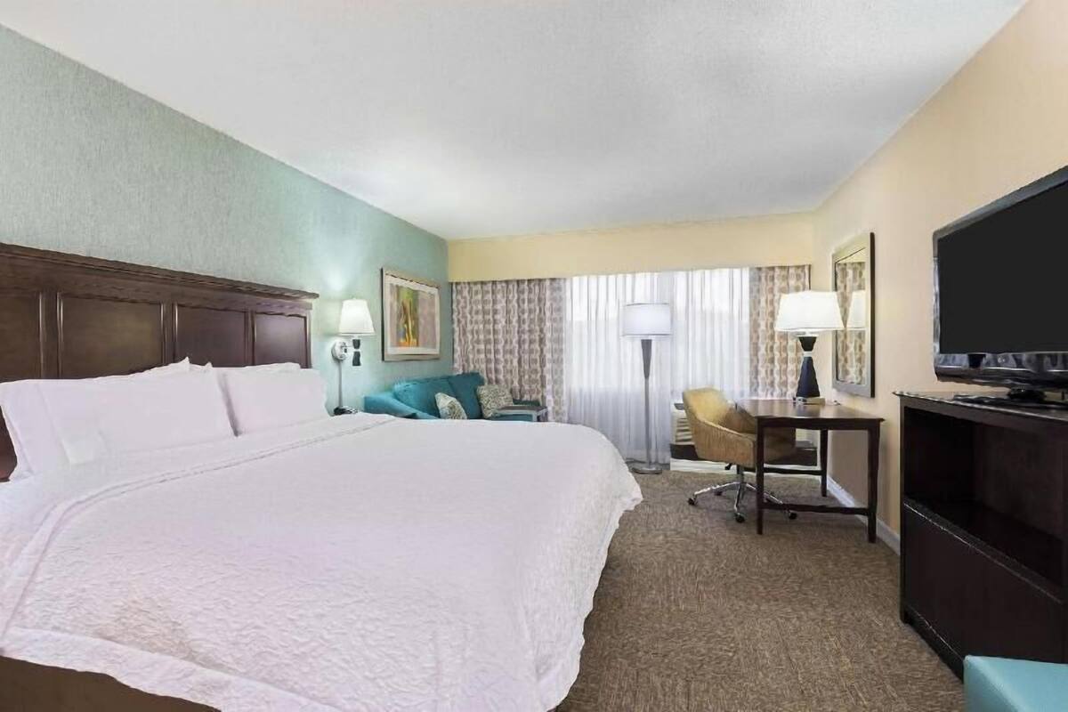 Une chambre d’hôtel avec un grand lit, un bureau avec une chaise, une télévision et une fenêtre avec des rideaux.