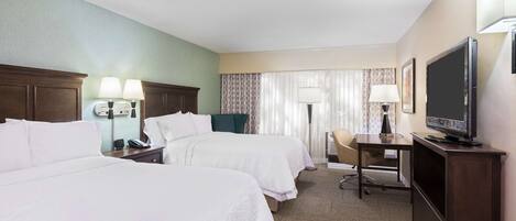 A hotel room with two beds, a desk with a chair, a television, and a lamp.