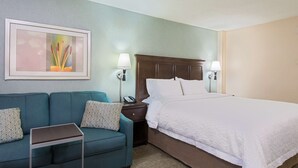 Ein Hotelzimmer mit Bett, Sofa, Nachttisch, Lampe und einem gerahmten Bild an der Wand.