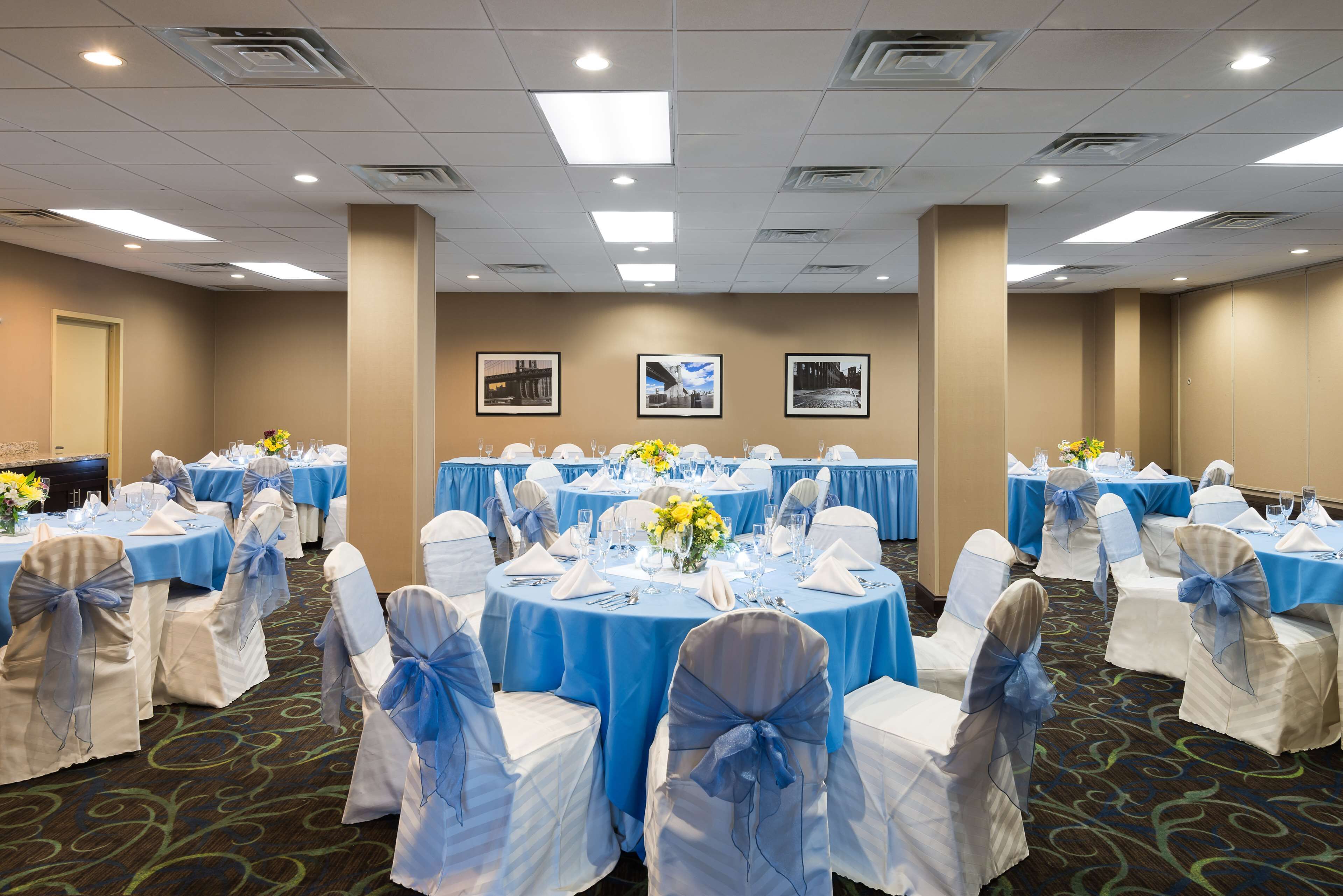 A banquet hall with round tables, white chairs with blue sashes, and floral centerpieces.