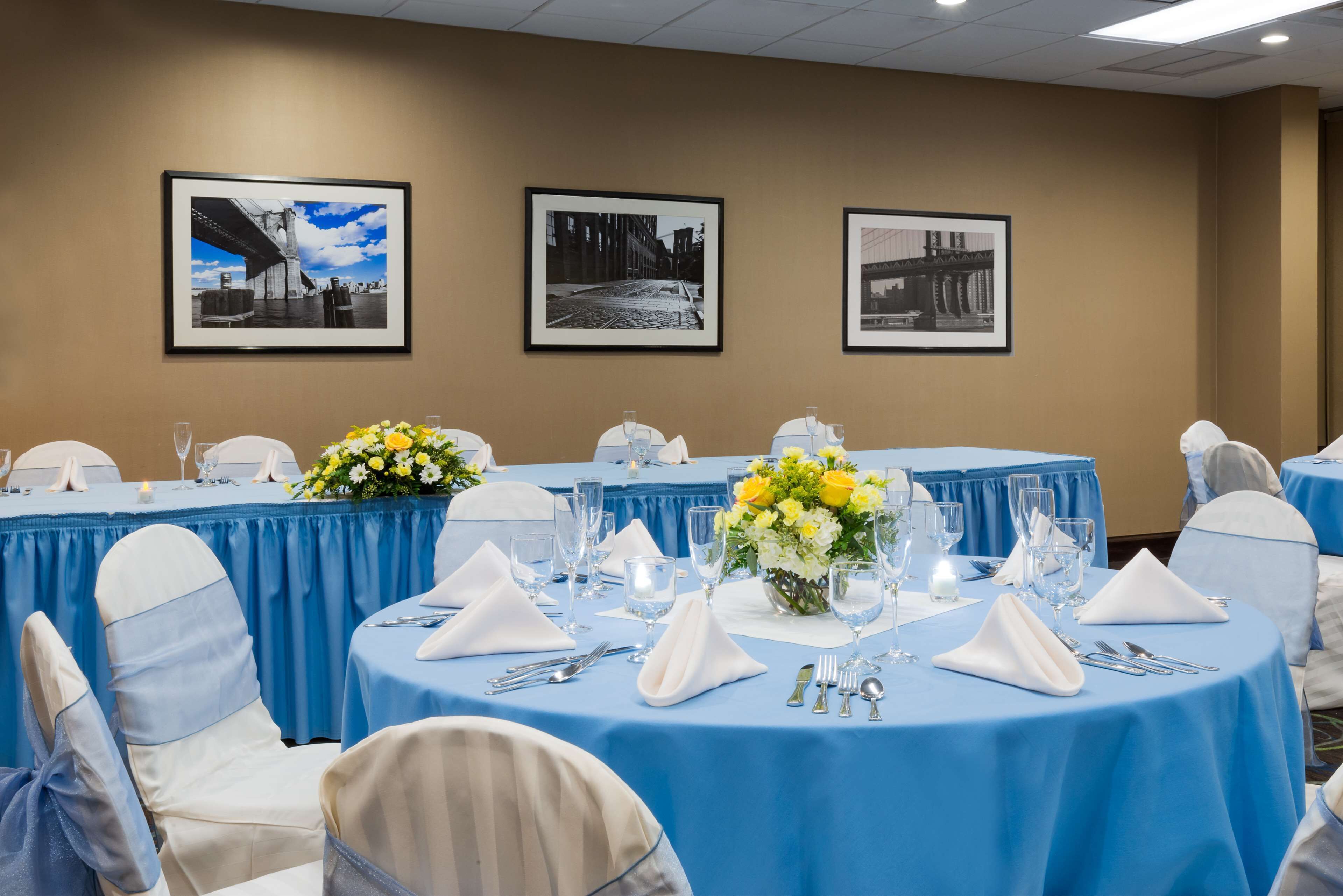 A conference room with round tables, blue tablecloths, white chairs, and framed black and white photographs on the wall.