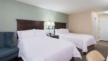 A hotel room with two beds, a desk with a lamp, a chair, and a door.