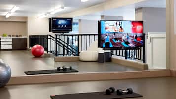 A modern fitness room with exercise equipment, a large mirror, and a television displaying fitness programs.