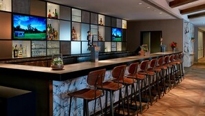 Een bar met een lange toonbank, meerdere televisies en een divers assortiment flessen en glazen.