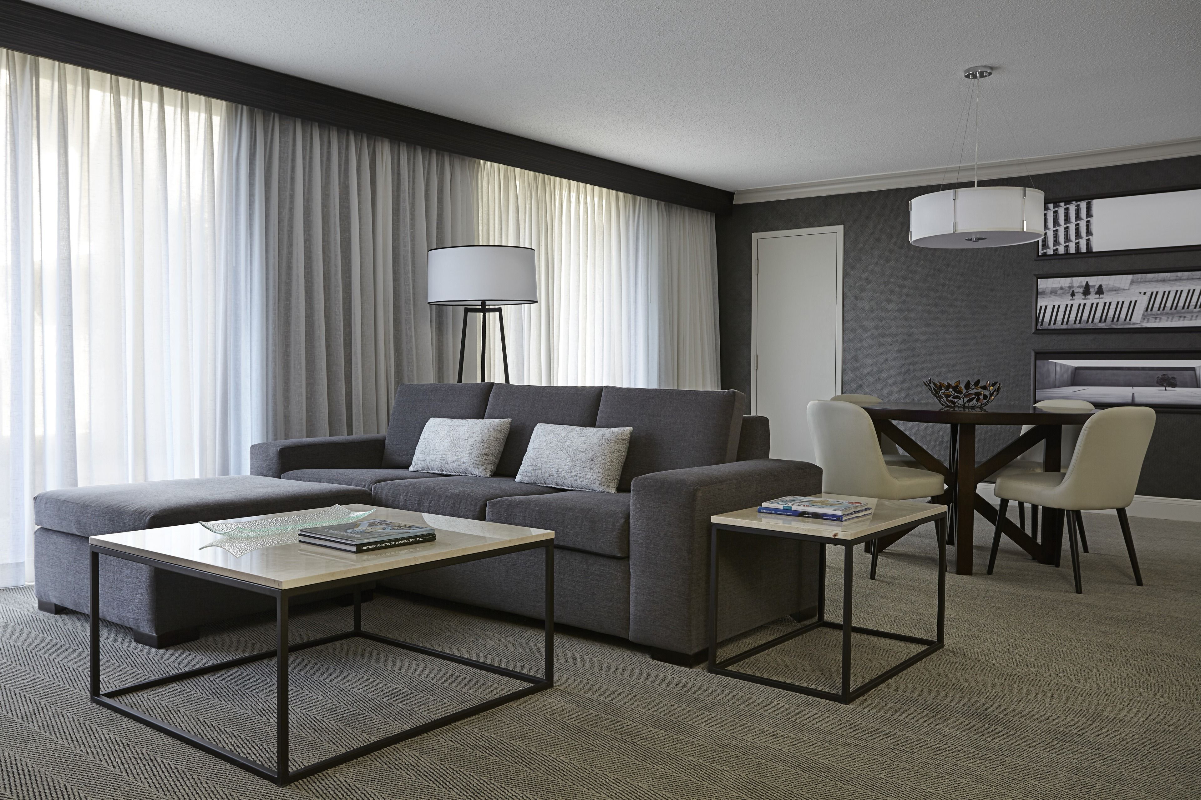 A modern living room with a grey sofa, a coffee table, and a dining area with a table and chairs.