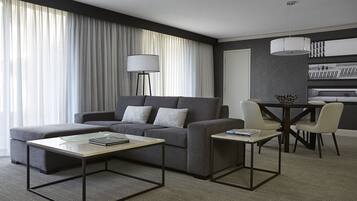A modern living room with a grey sofa, a coffee table, and a dining area with a table and chairs.