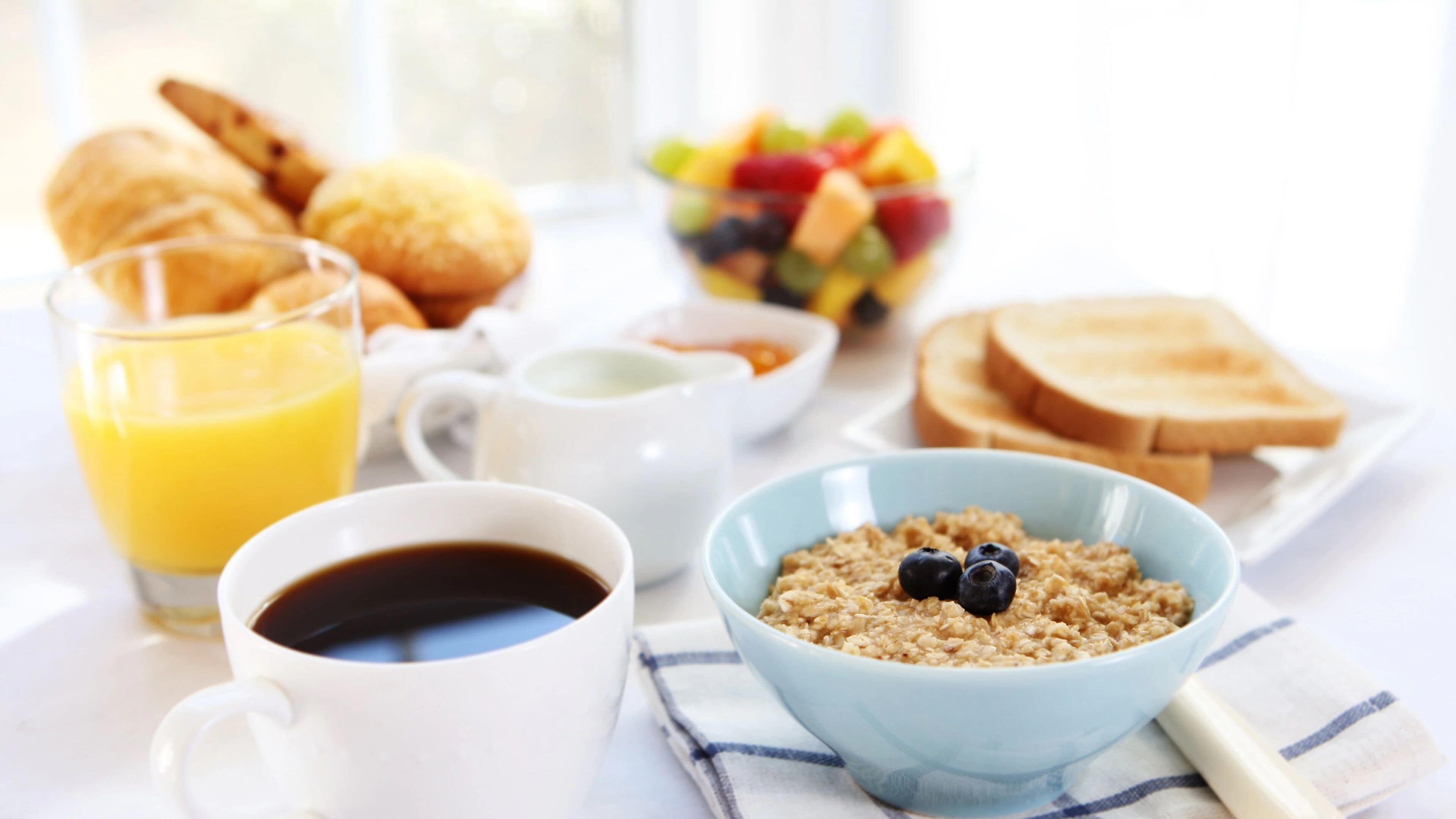 A breakfast setting with a bowl of cereal, toast, a glass of orange juice, a cup of coffee, and pastries.