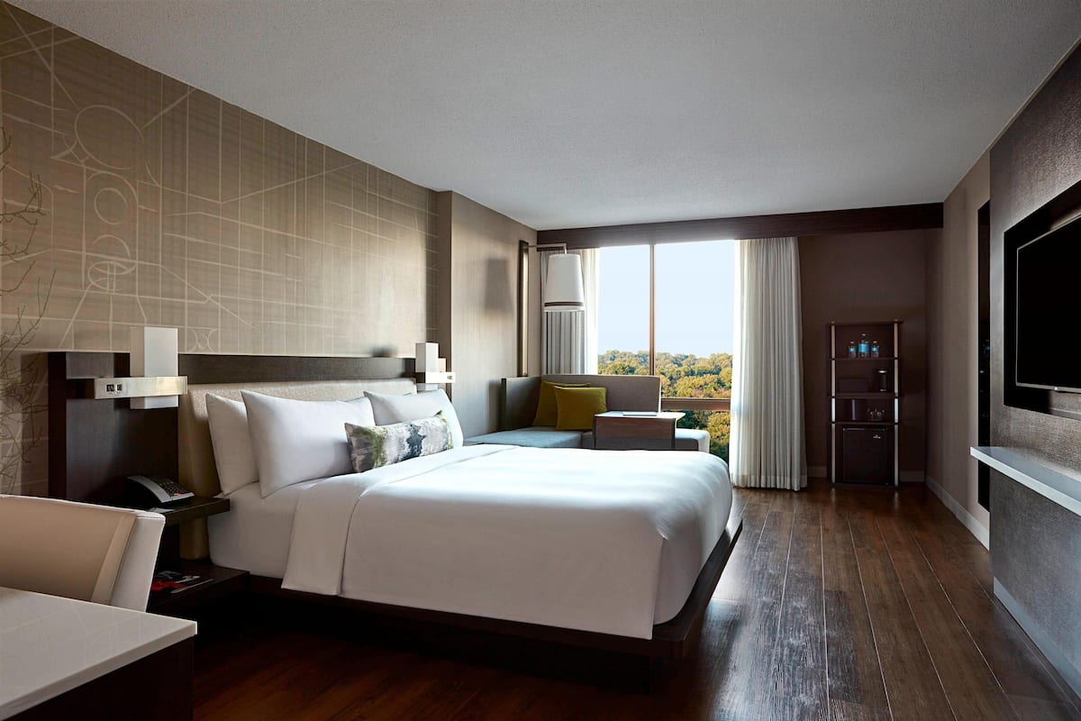 A hotel room with a large bed, bedside tables, a desk, a TV, and a view of the outdoors.