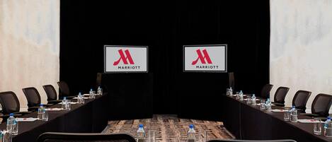 A conference room with a long table, black chairs, water bottles, and Marriott logos on the back wall.