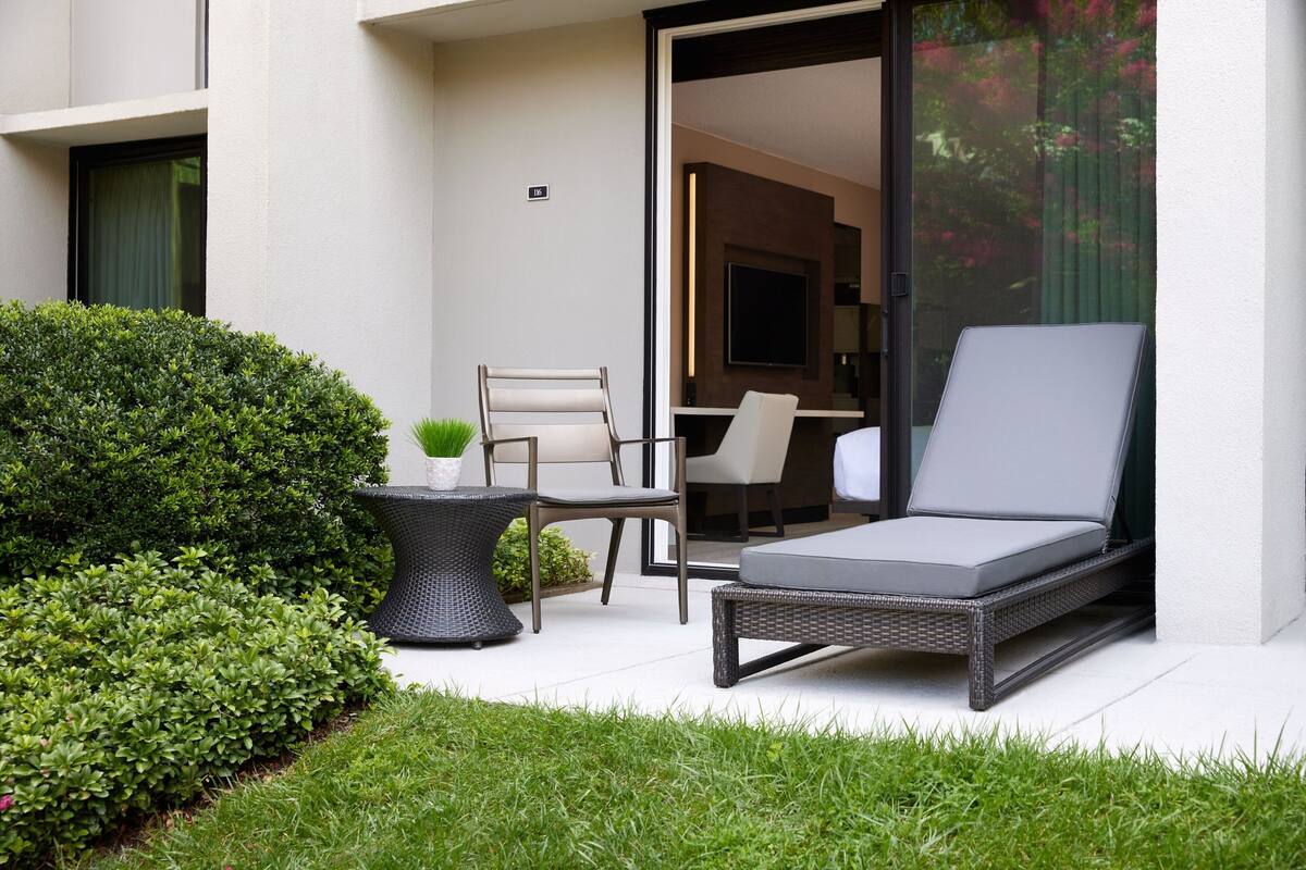 A modern outdoor seating area with a lounge chair, a table, and a chair, surrounded by well-maintained greenery.