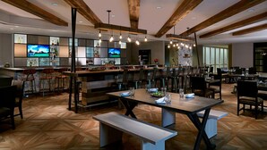 Een modern restaurant met houten balken, een bar en een eetgedeelte met tafels en stoelen.