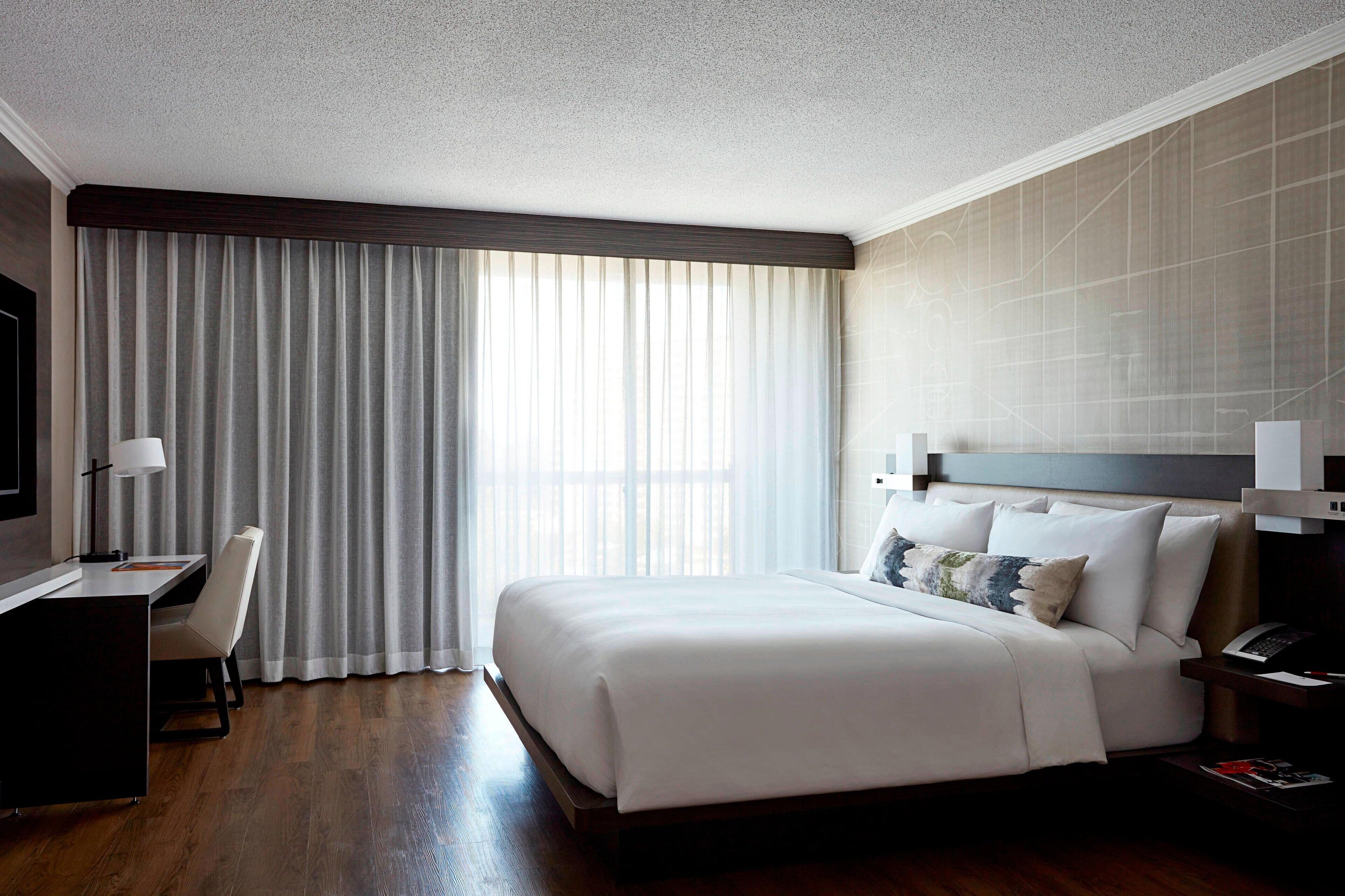 Una habitación de hotel con una cama grande, un escritorio con silla, televisión y una ventana con cortinas.