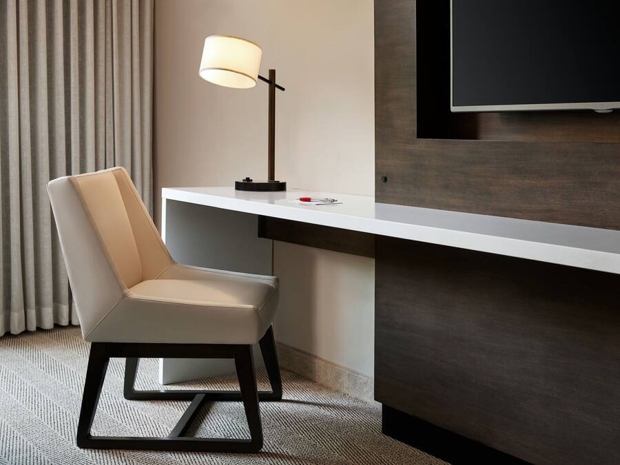 Una habitación de hotel moderna con escritorio, silla, lámpara y televisor de pantalla plana montado en la pared.