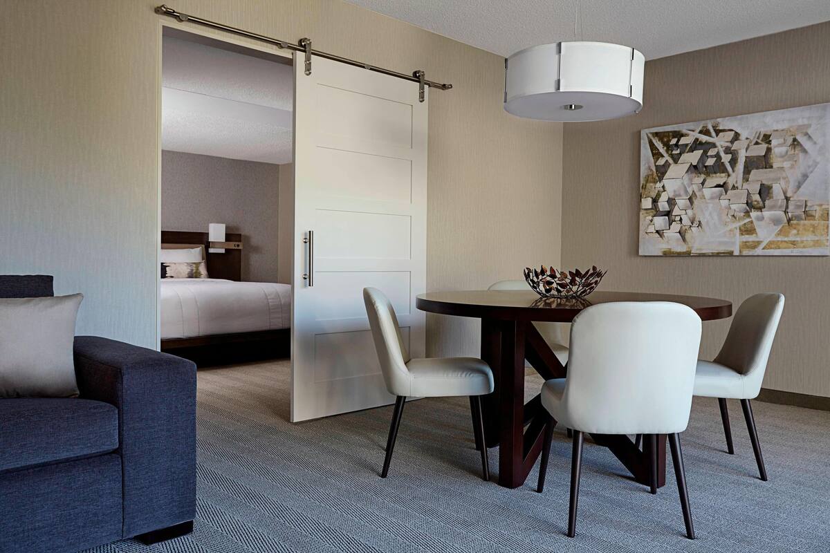 A hotel room with a bed, a sofa, a dining table with chairs, and a painting on the wall.