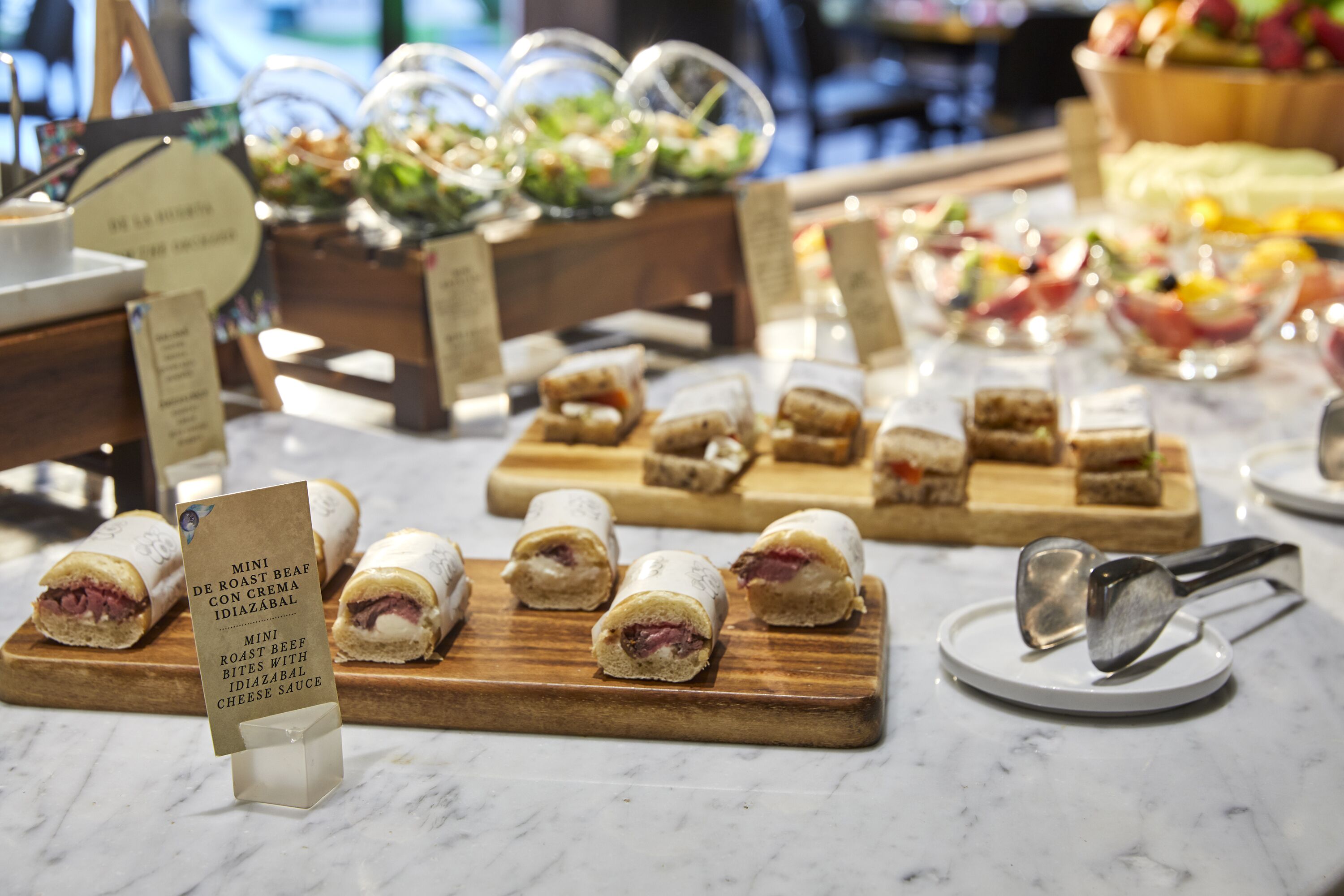 Una mesa de buffet con diversos alimentos, incluyendo bocados de roast beef con salsa de queso Idiazabal.