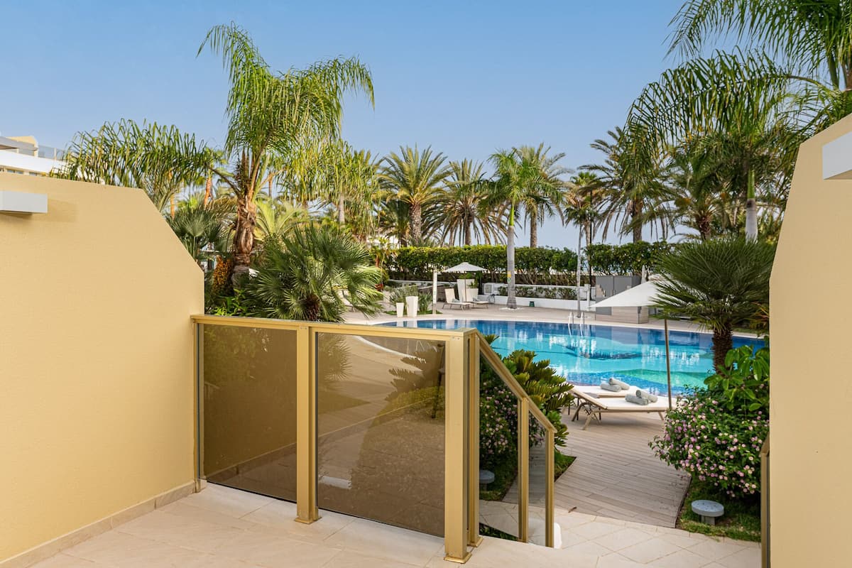 A pool area with a clear view of the pool, lounge chairs, and surrounding palm trees.