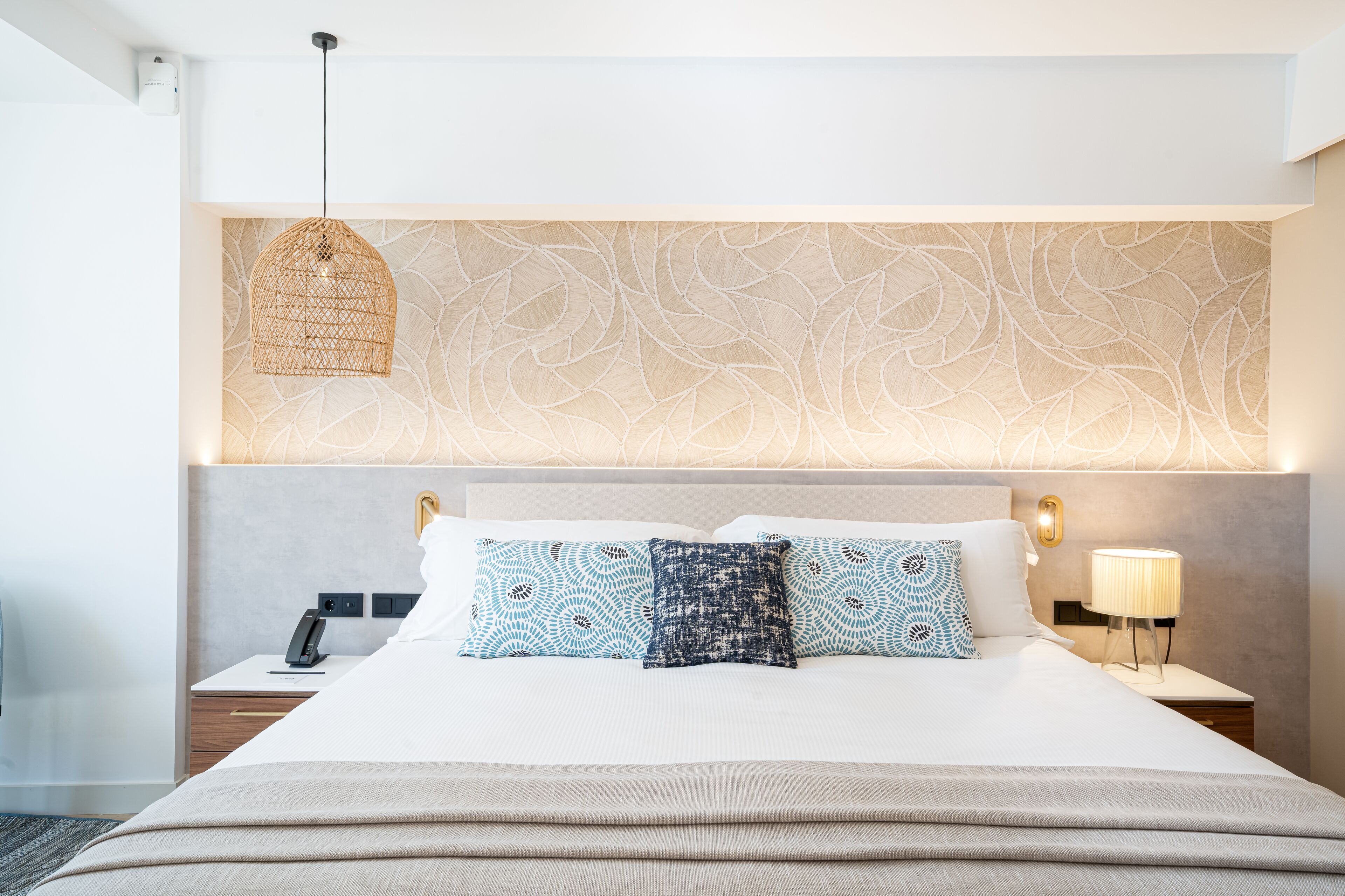 A modern hotel room with a large bed, a nightstand, a lamp, and a decorative wall panel.