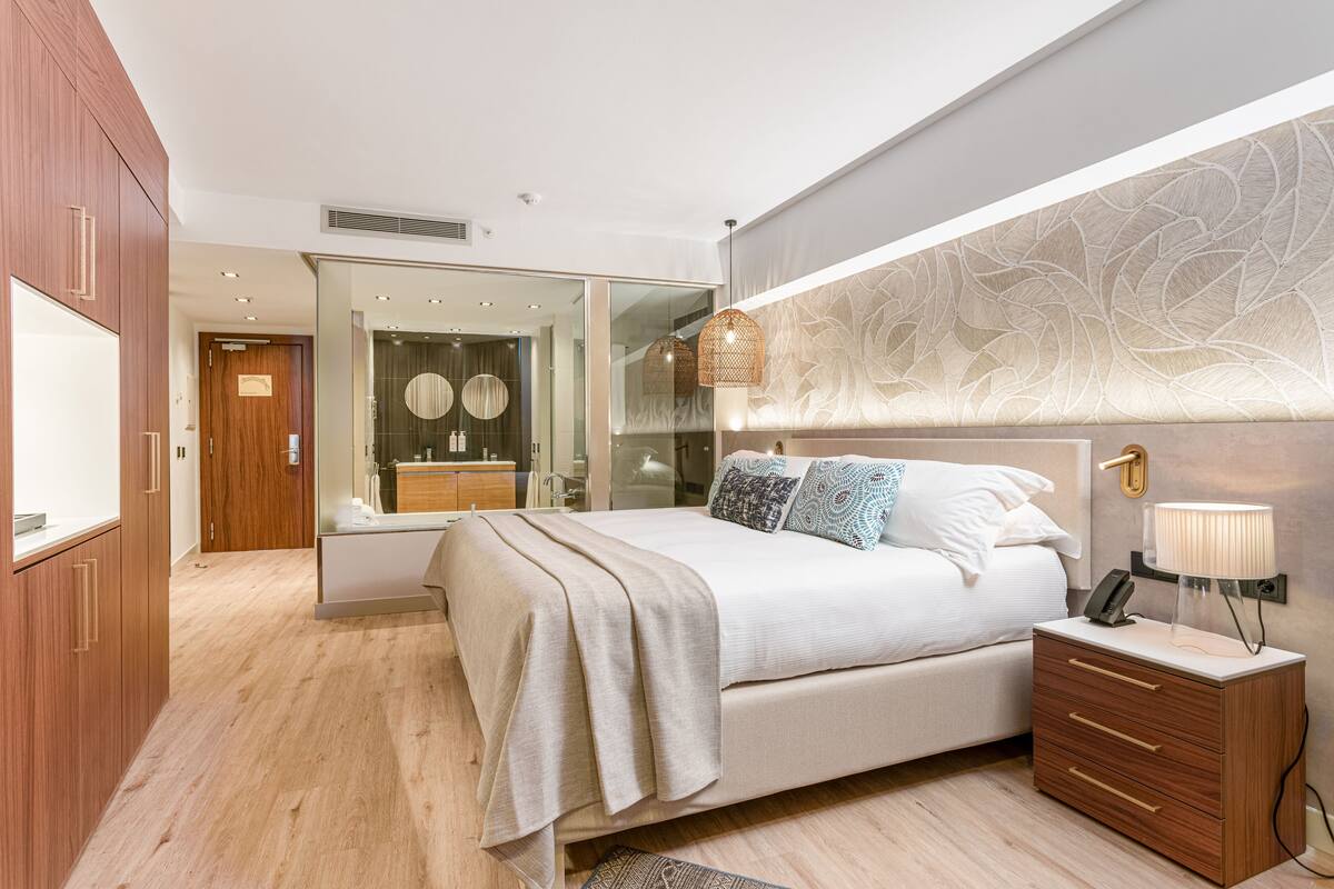 A modern bedroom with a bed, bedside table, and a mirror.