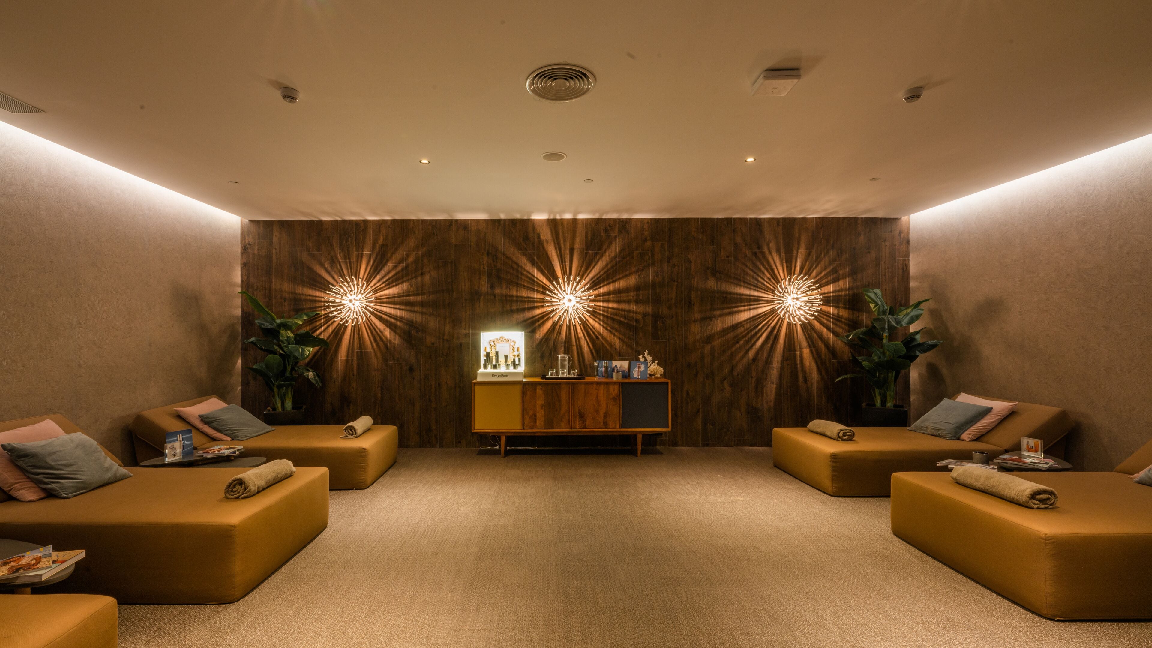 Un cuarto de spa con dos camillas de masaje, una pared de madera con iluminación tipo estrella y un mostrador de recepción, además de una planta en maceta.