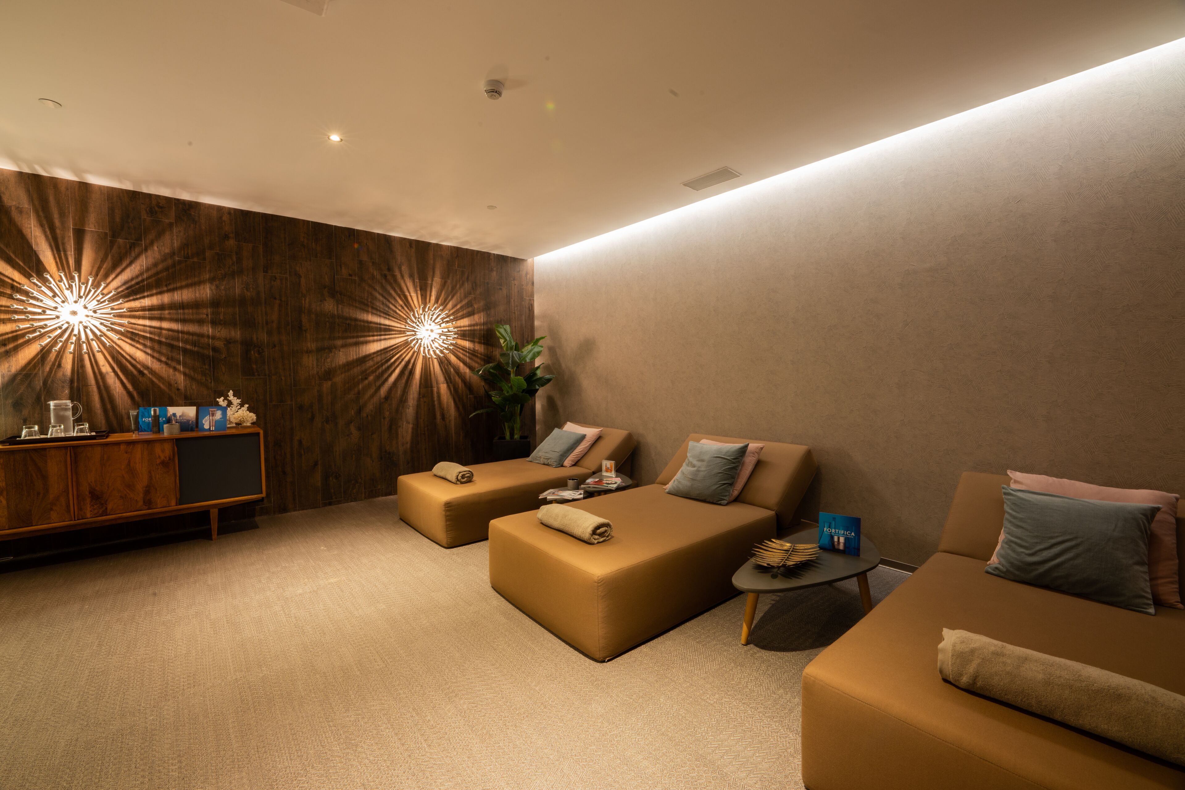 A modern spa room with two sofas, a wooden cabinet, and a small table with amenities.