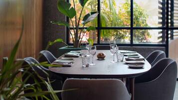A dining table set for six with plates, glasses, and cutlery, positioned near a window with a view of greenery.