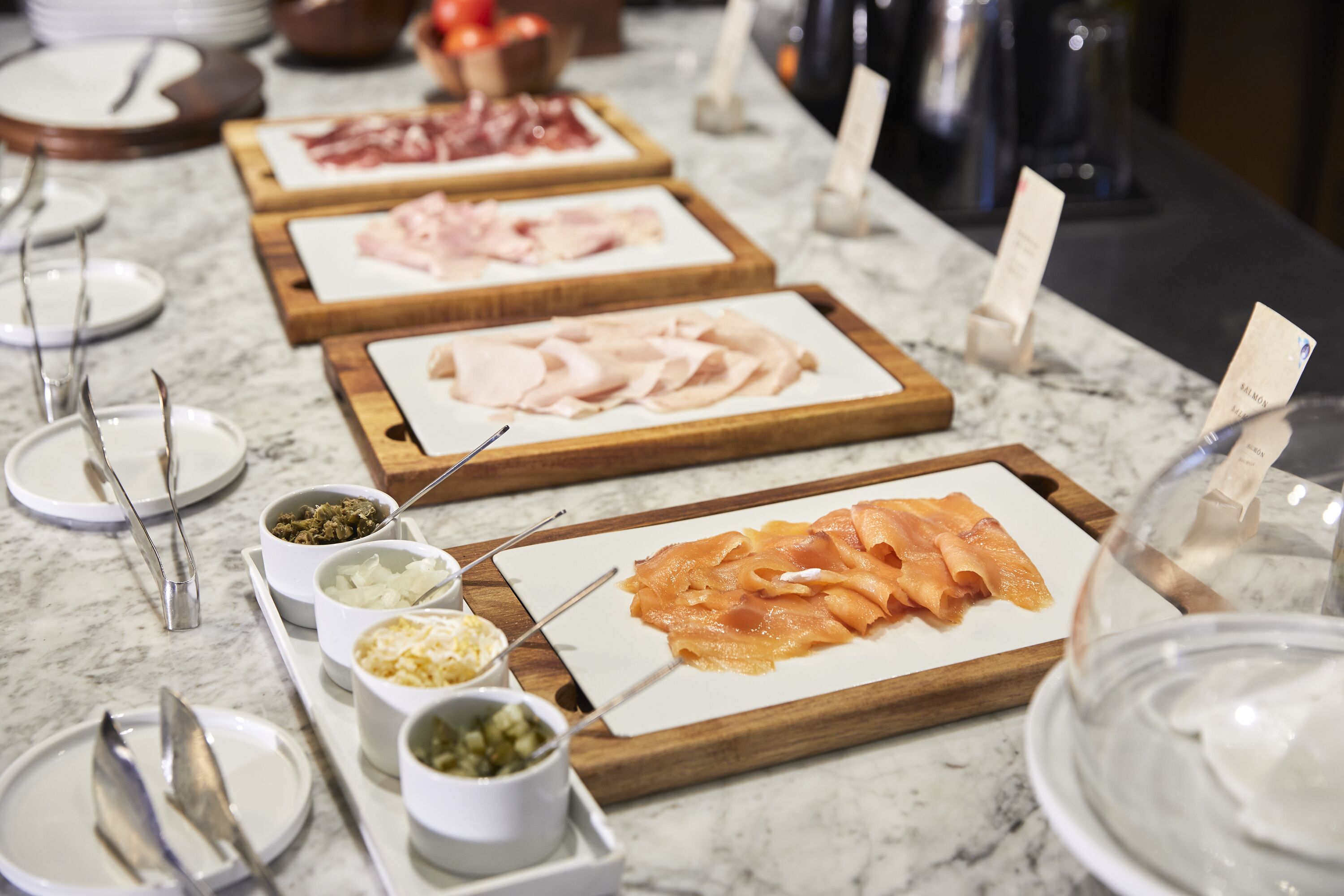 A buffet with various meats and condiments on wooden boards.