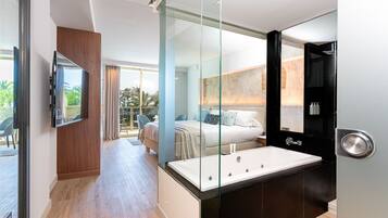 A modern hotel room with a large bed, a glass-enclosed shower, and a flat-screen TV mounted on the wall.