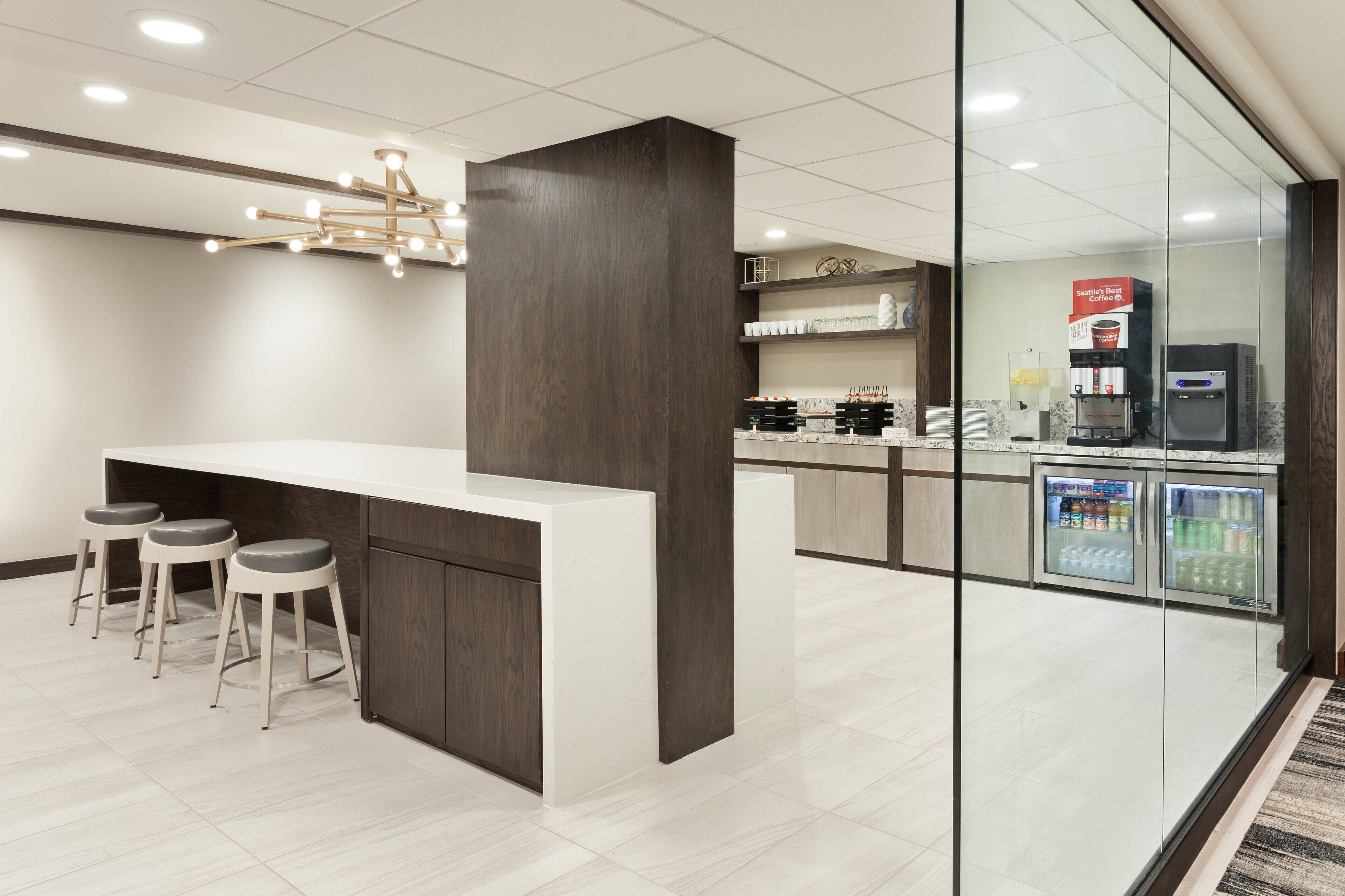 A modern kitchen with a bar area, stools, a coffee machine, and a refrigerator.