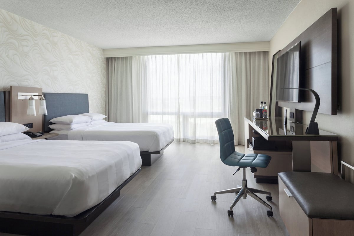 Habitación de hotel con dos camas, un escritorio con silla, televisión y minibar.