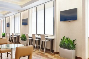 Uma sala de conferências moderna com mesas de vidro, cadeiras brancas e plantas em vasos.