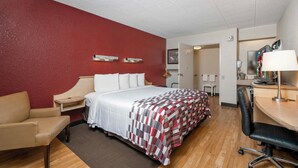 A hotel room with a bed, a desk, a chair, a desk lamp, a TV, and a bathroom visible through an open door. - Red Roof Inn Louisville Expo Airport (Louisville)