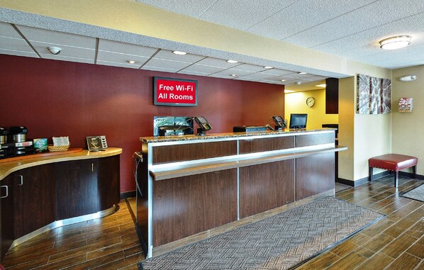 A hotel reception area with a red wall, a digital clock, and a sign indicating free Wi-Fi availability.