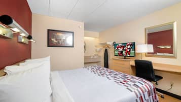 Habitación de hotel con cama, escritorio, televisor, espejo y lámpara de pared.